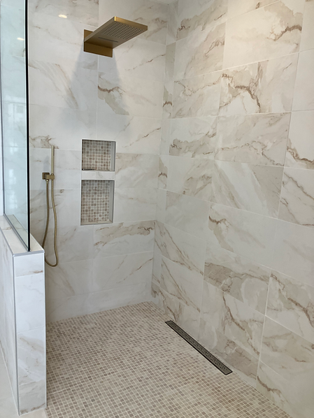 Modern walk-in shower with marble tiles and gold hardware.