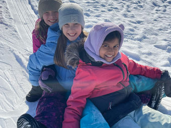 Three happy children sledding together down a bright snowy slope.