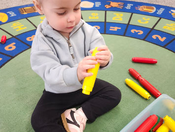 Toddler playing with yellow crayon toy on a colorful rug.
