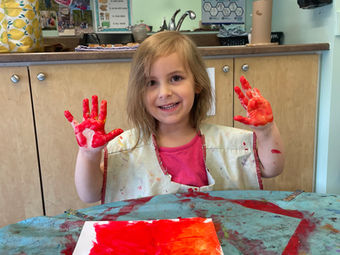 Smiling young girl proudly shows red painted hands and artwork.