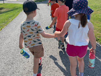 Young children holding hands, walking on a paved path outdoors.