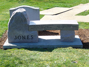 Stone memorial bench with "JONES" carved, set in a grassy area.