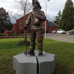 Bronze statue of soldier in military uniform holding rifle, outdoor monument.
