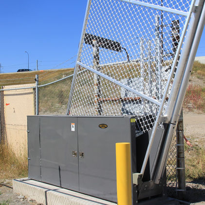 Outdoor electrical box with fence, road and a truck on a sunny day.