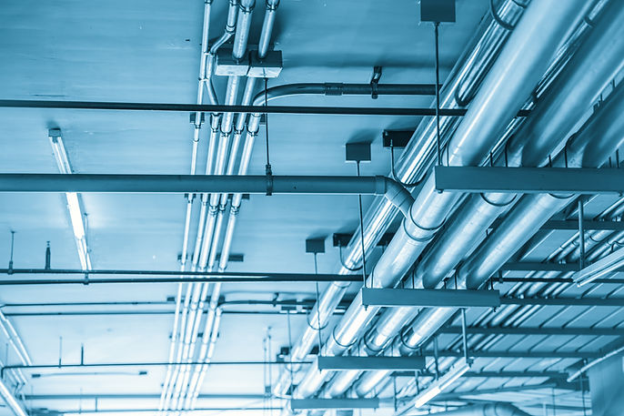 Industrial pipes and electrical conduits mounted on a blue-tinted ceiling.