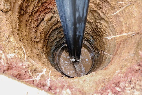 Drilling rig bit digging a deep, wet hole in brown earth.