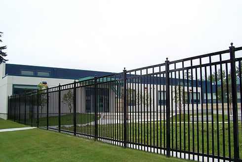 Black metal fence surrounding the building with green grass and overcast sky.