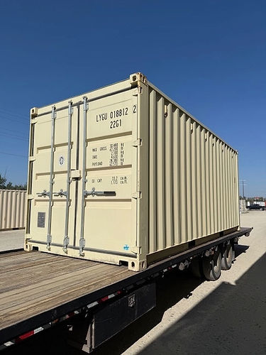Beige shipping container on a flatbed trailer under a clear blue sky