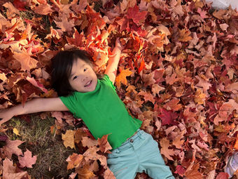 Young child happily laying in vibrant autumn leaves, smiling and relaxed.