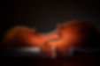 Wooden cello body, F-holes, bridge, and strings illuminated by soft light.