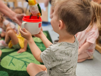 Young boy holding colorful toy bird on red cup in classroom.