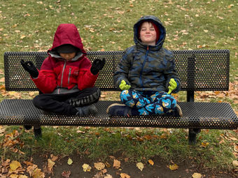Two children meditating calmly on a park bench during autumn.
