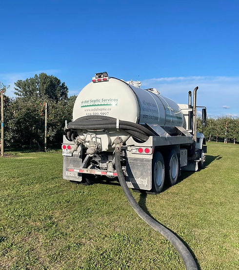 Septic tank service truck pumping on a grassy field.