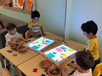 Four children playing with colorful shapes on two light tables.