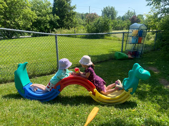 Two children playing on a colorful seesaw outdoors on a sunny day.
