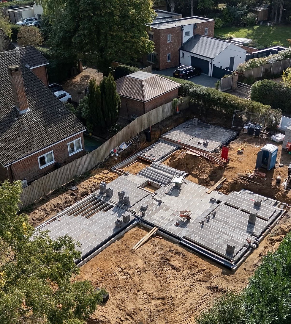 Aerial view of a suburban home construction site with concrete foundations, dirt lot, and a blue portable toilet; DAVISON watermark.
