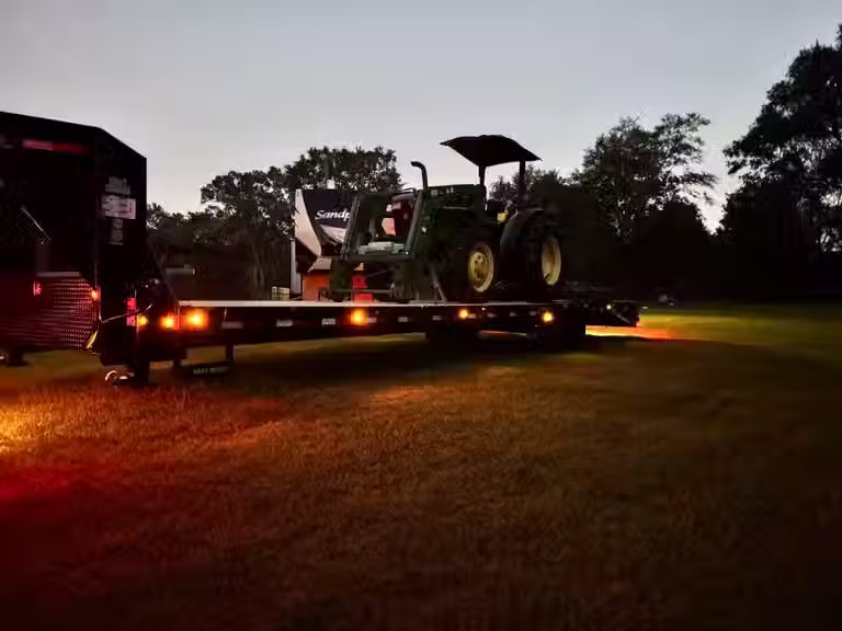 Green tractor with shredder attachment loaded on a trailer