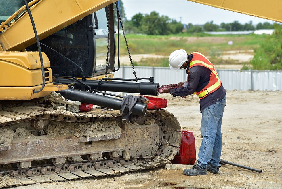 Worker inspecting and maintaining the hydraulic cylinders of a construction excavator on a job site.
