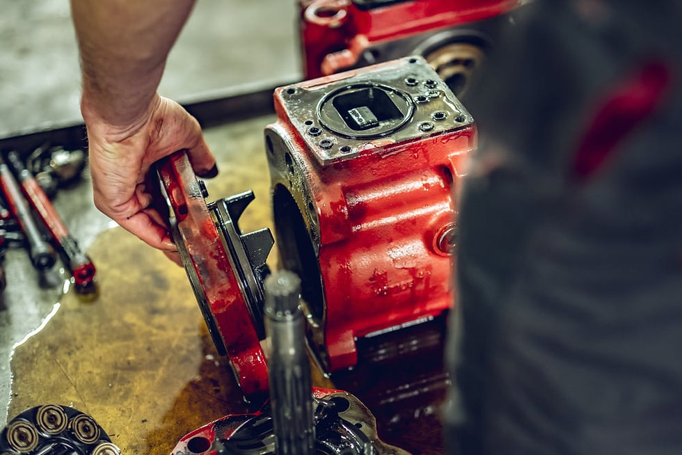 A close-up of a hydraulic specialist disassembling a red hydraulic pump for repair and inspection, with tools and components visible in the background.