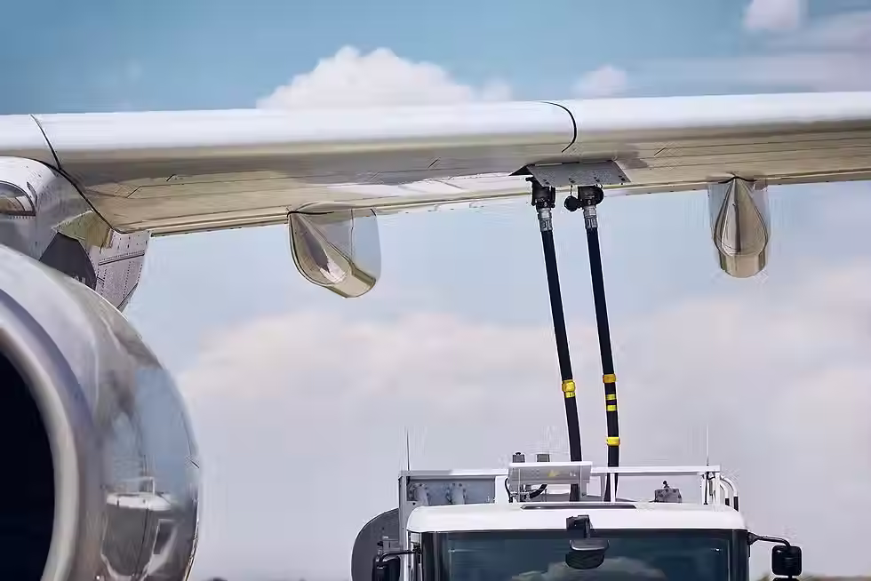 An aircraft maintenance technician inspecting the underside of an airplane in a hangar, holding a clipboard for documentation.