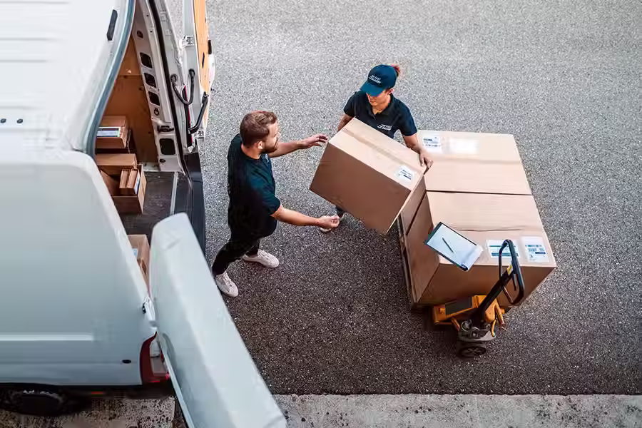 Two delivery workers unloading boxes from a van, ensuring timely industrial tool delivery for manufacturing needs.