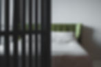 Green headboard and white bed partially visible behind black vertical bars, in a minimalistic bedroom with a calm, muted tone.