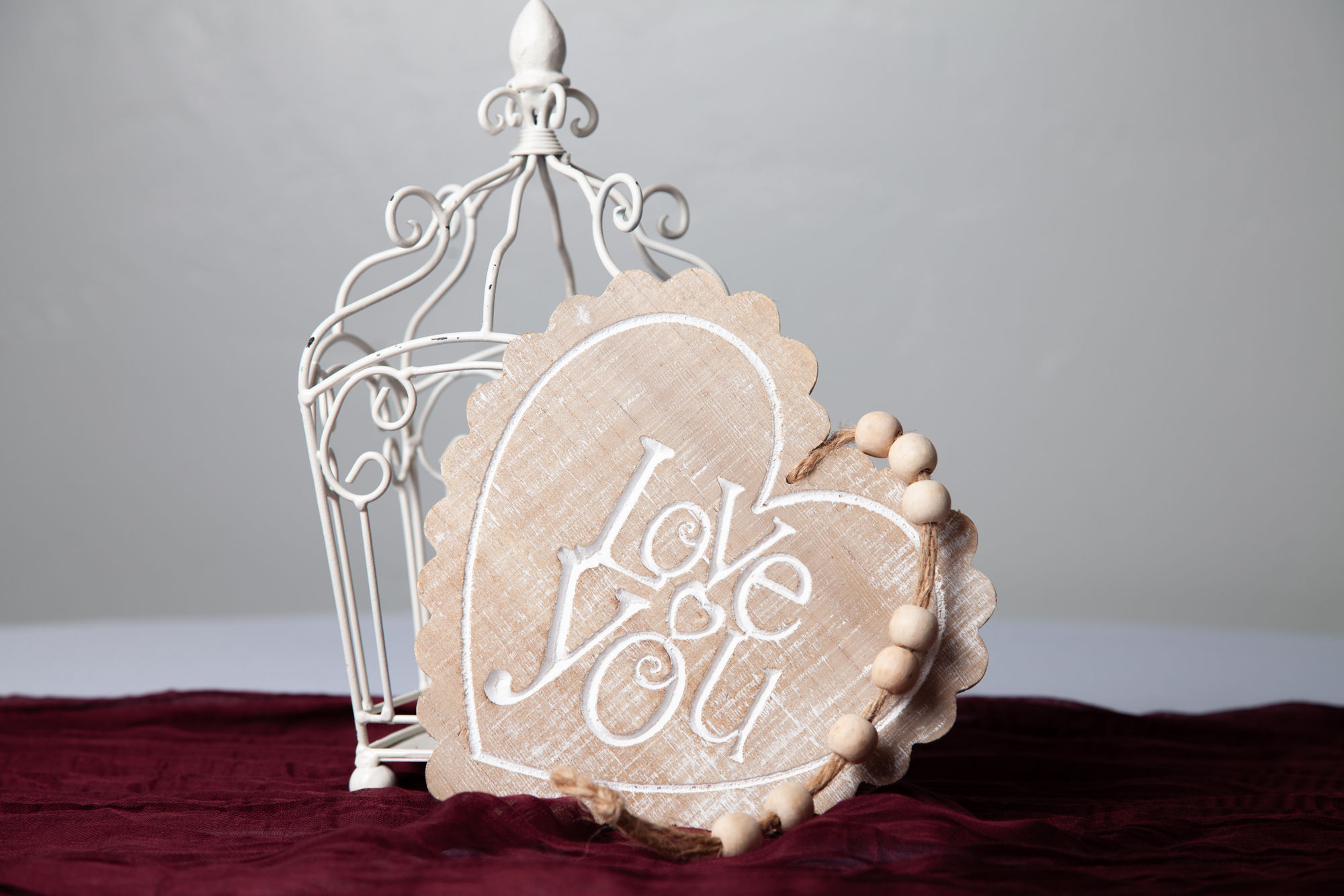 Wood heart sign with scalloped edge, white 'Love You' script, and bead accent, styled with white scroll centerpiece frame.