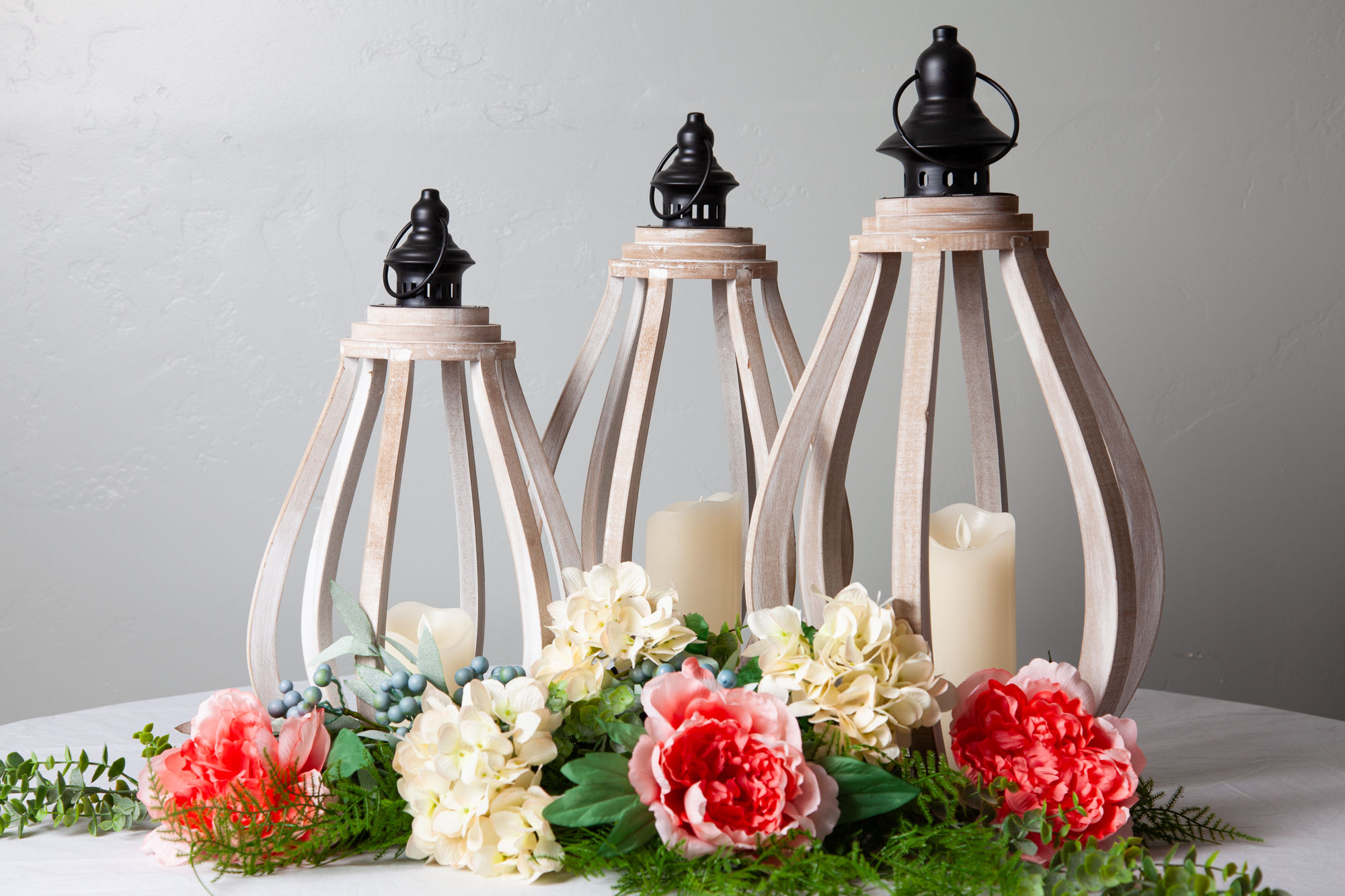 White wood lanterns in three sizes with pillar candles and floral accents, perfect for wedding aisle or entry decor rentals.