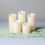 Thumbnail: Set of ivory flameless pillar candles in varying heights, styled on a green runner—perfect for elegant wedding centerpieces.