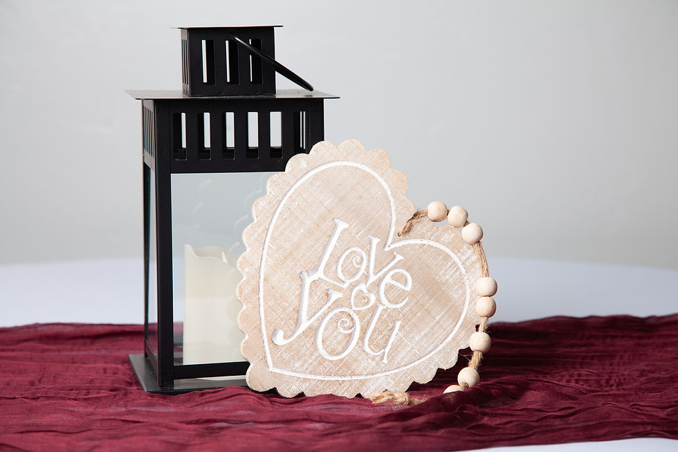 Love You wood heart sign with white script and wood bead detail, styled next to black lantern for wedding or event decor.
