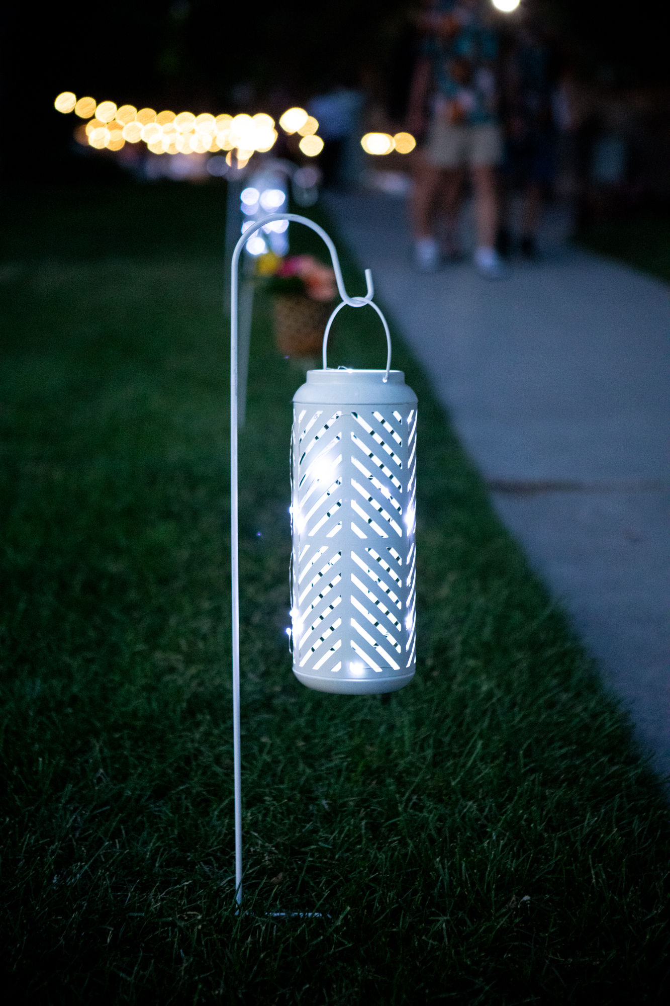 White LED cylinder lantern hanging from shepherd hook, glowing softly at night.