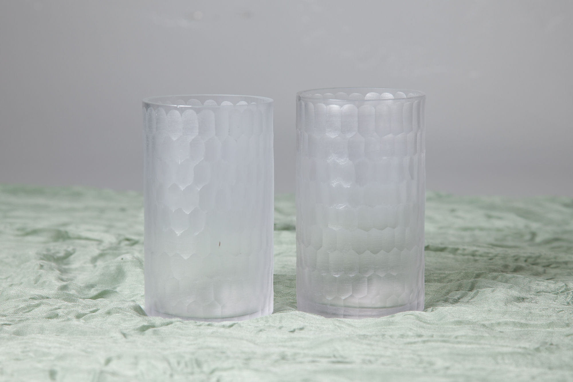 Pair of frosted glass cylinder vases on soft green fabric, perfect for wedding candles or minimalist floral accents.