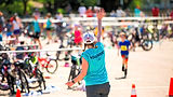 Excited child raising hand at the start of a kids’ triathlon event, with bikes and athletes in the background