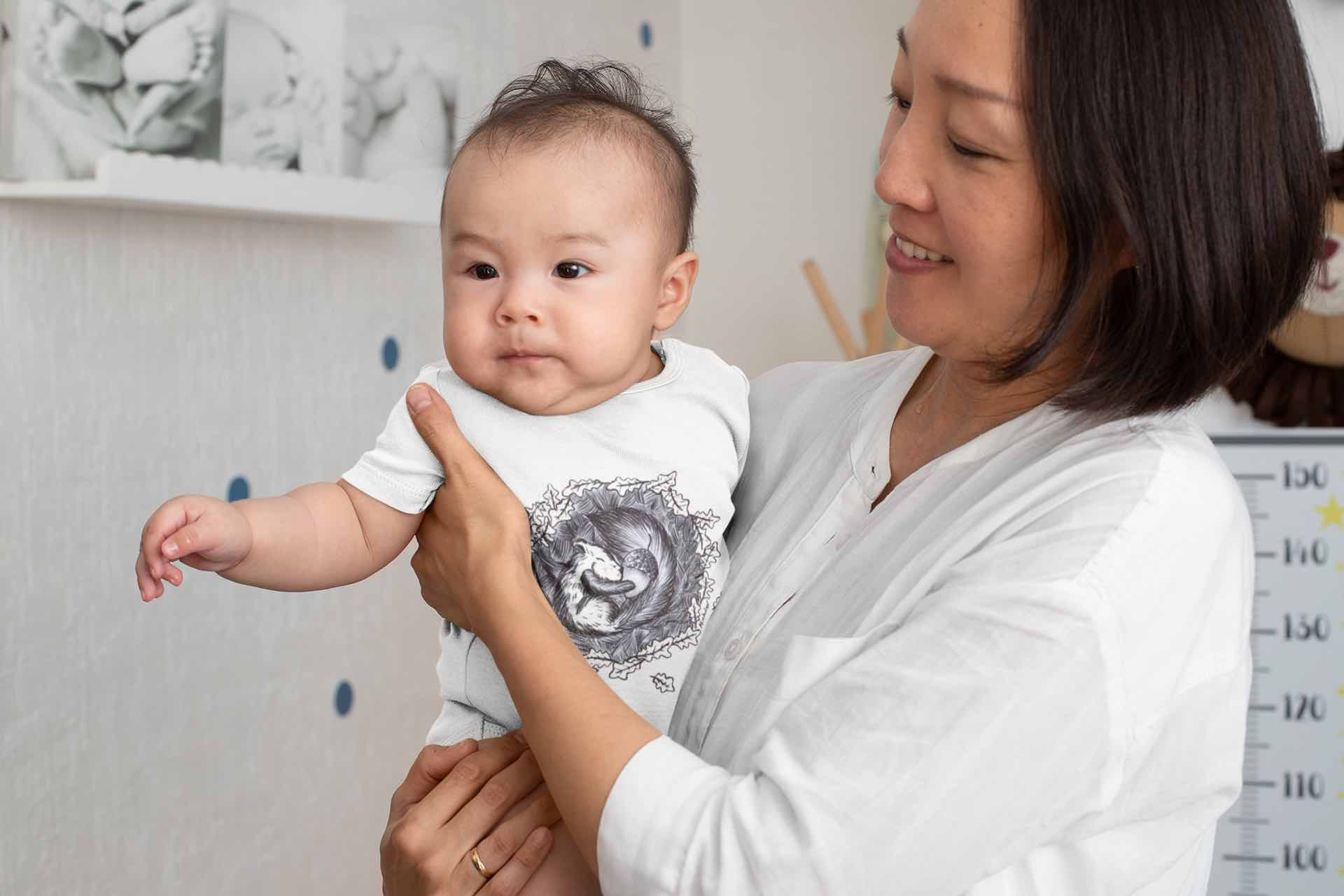Woman holds baby in white bodysuit with Squirrel graphic.
