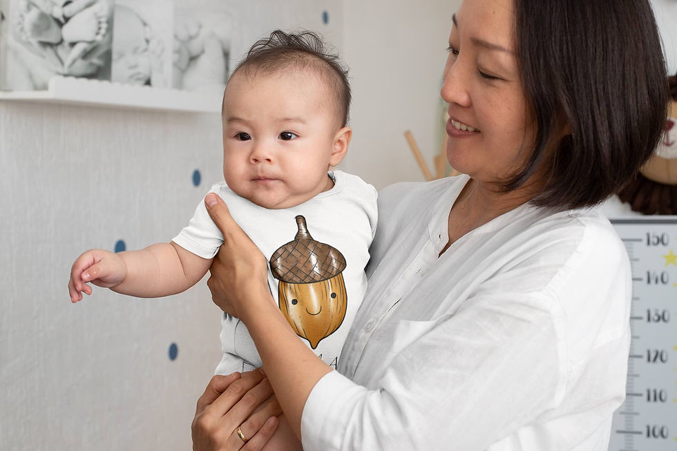 Baby held by adult, wearing white "Little Acorn" bodysuit.
