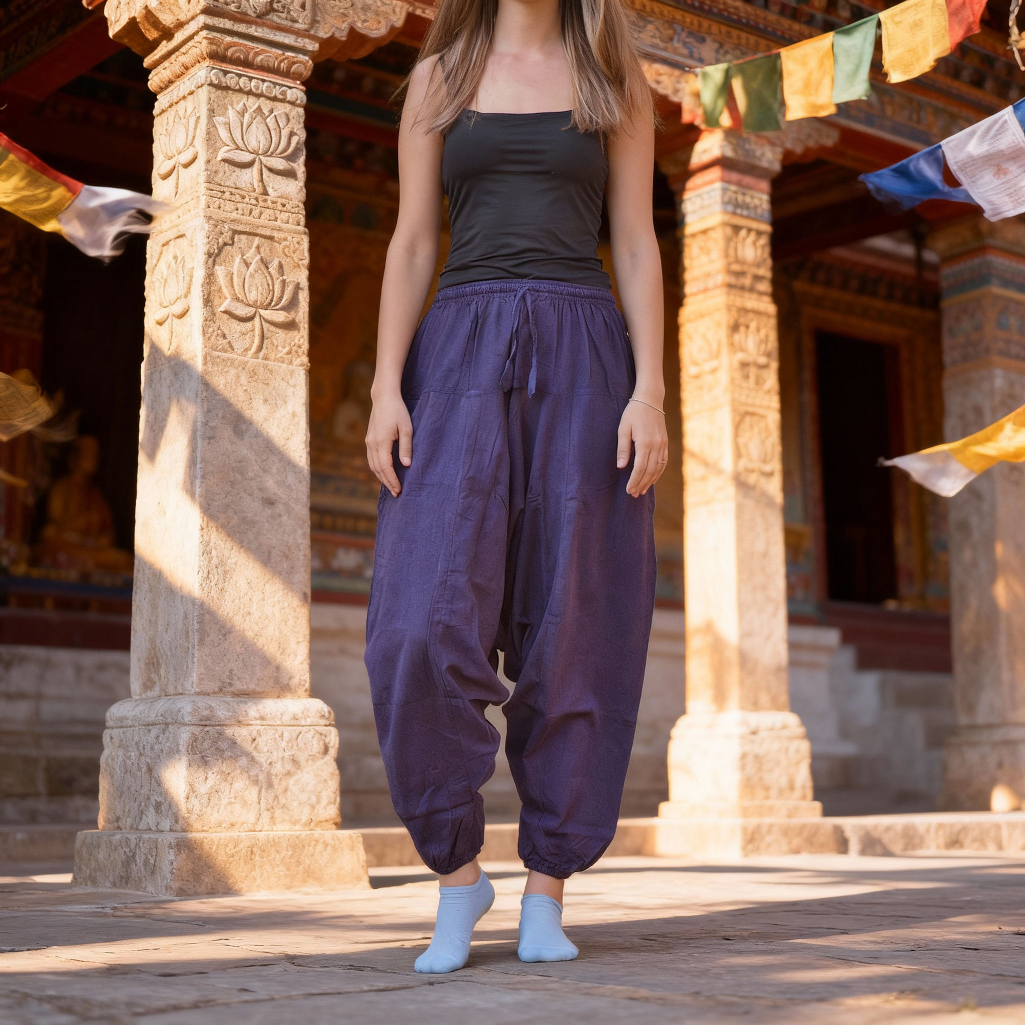 Persona in piedi con pantaloni aladdin di cotone viola con coulisse, in uno sfondo architettonico di pietra.