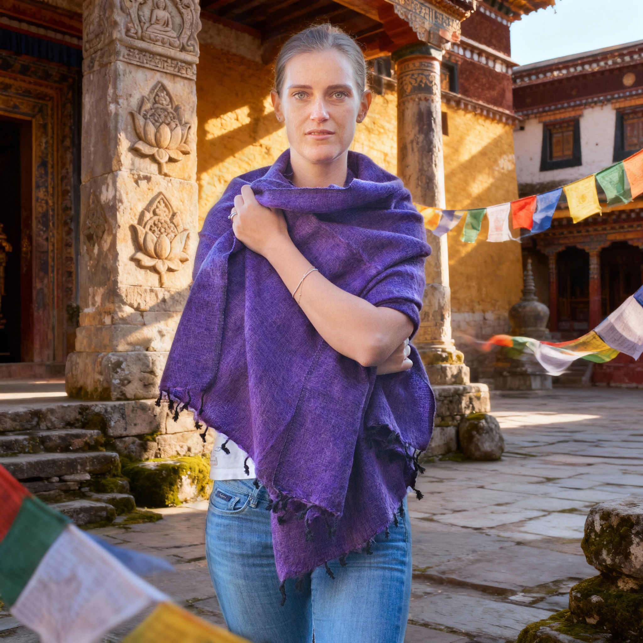 Donna con scialle in lana yak lavanda drappeggiato, frontale in cortile di pietra con bandiere di preghiera.