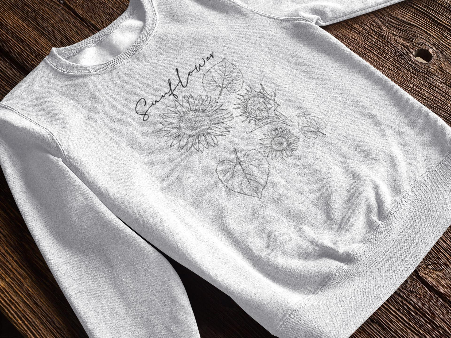 Grey sweatshirt with "Sunflower" text and greyscale sunflower and leaf outlines.