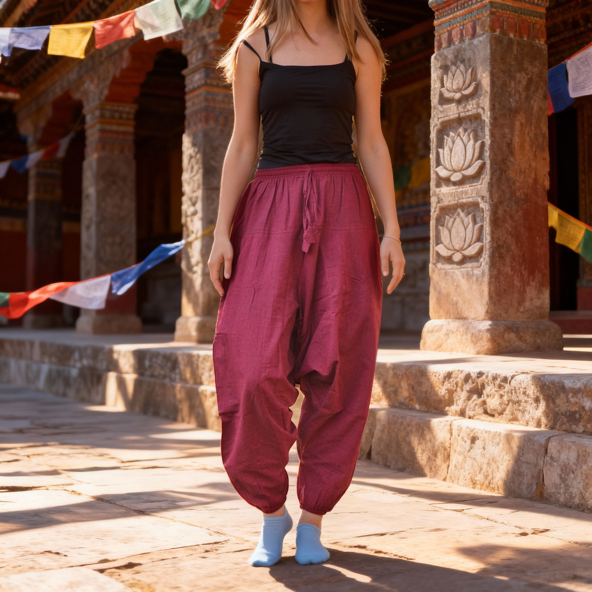 Persona in piedi con pantaloni aladdin di cotone bordeaux con coulisse, in uno sfondo architettonico di pietra.