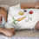 Thumbnail: Baby in white "Veggie Power" bodysuit, lying on textured surface.