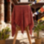 Sciarpa Om rosso vino drappeggiata su un supporto di legno in un cortile del tempio soleggiato.