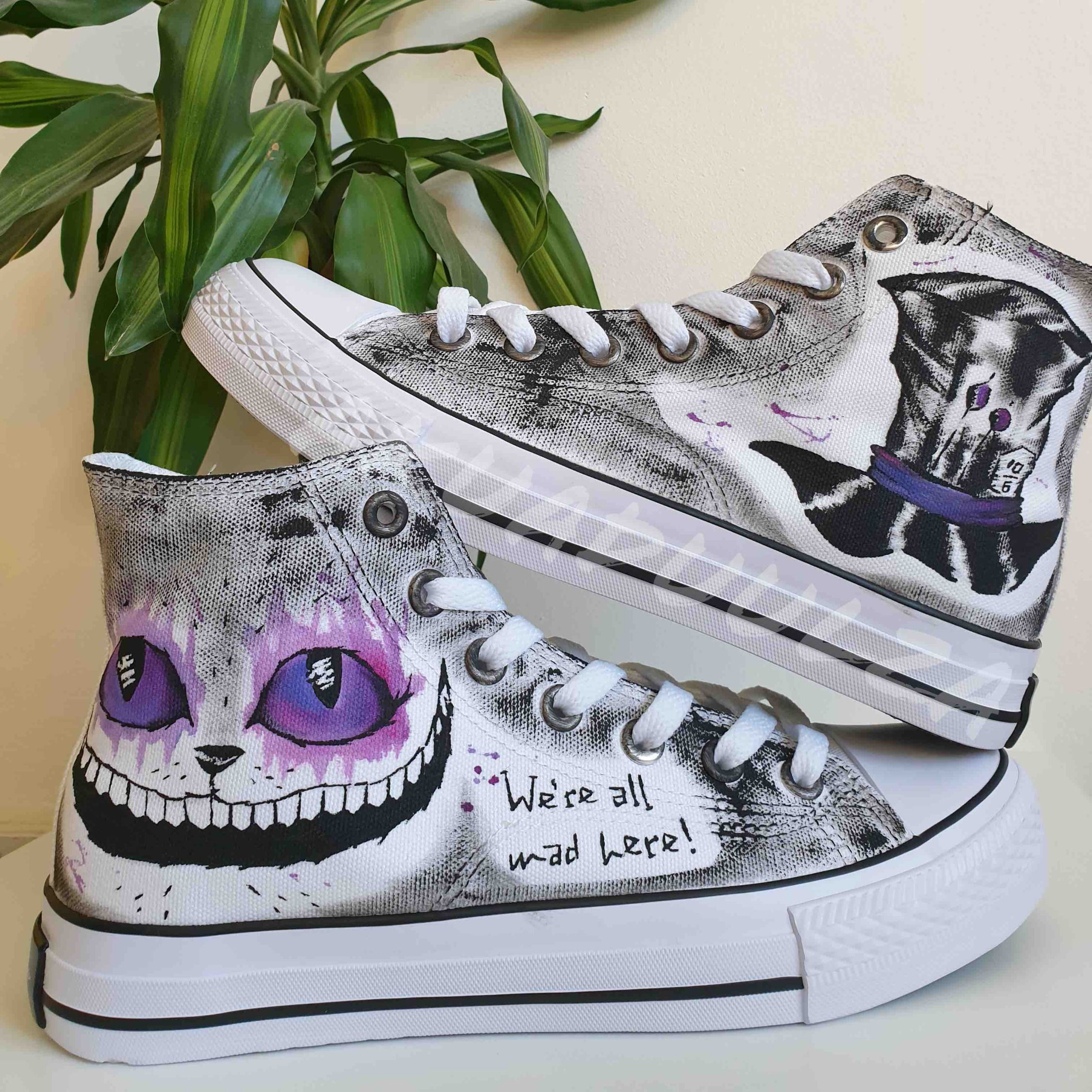 White high-top canvas shoes with handpainted Purple Cheshire cat and mad hatter, placed top of each other.