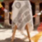 Sciarpa OM bianca drappeggiata su un supporto in legno in un cortile di pietra.