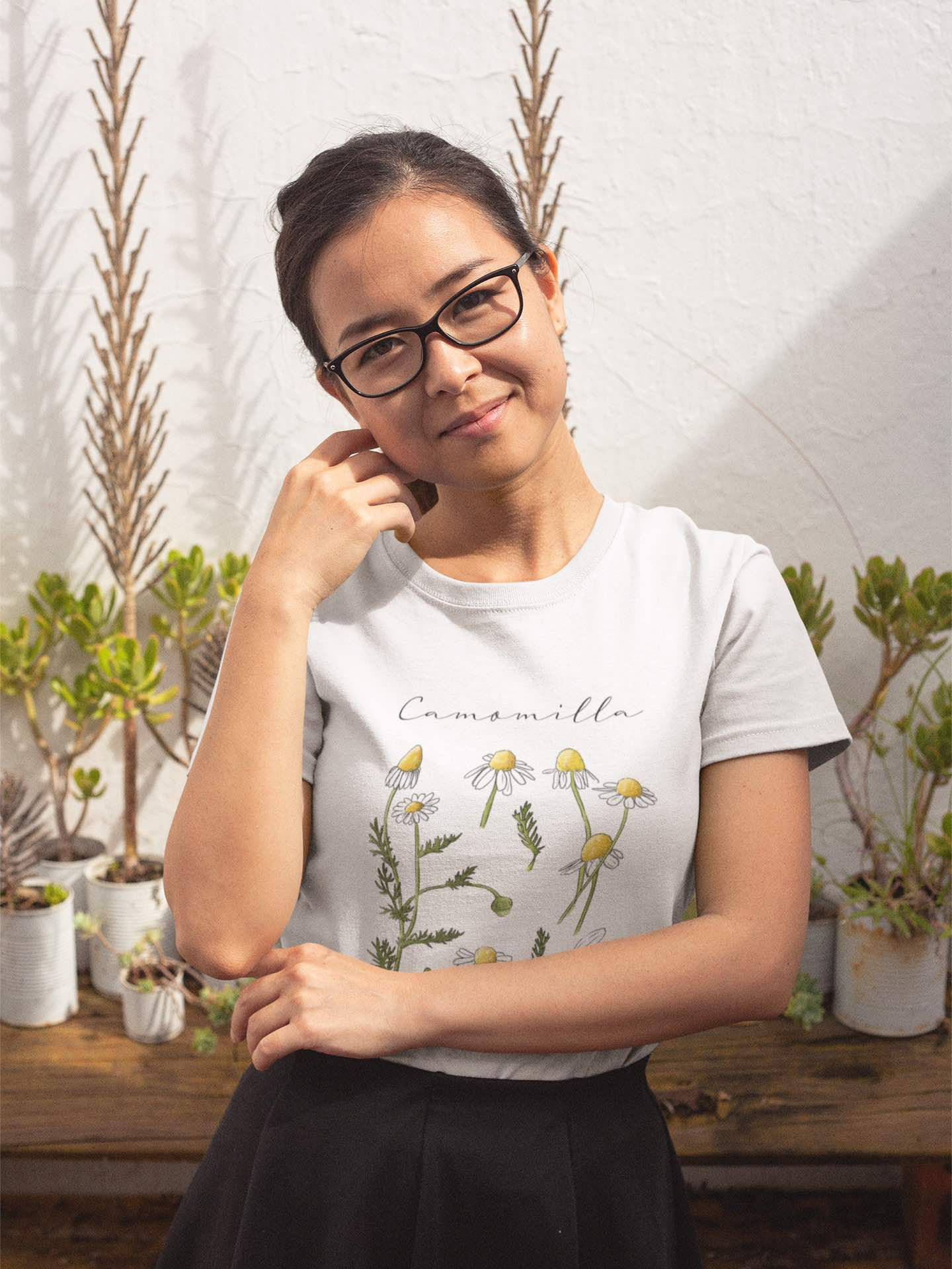 A woman in glasses smiles, wearing a "Camomilla" t-shirt with Camomile illustrations.