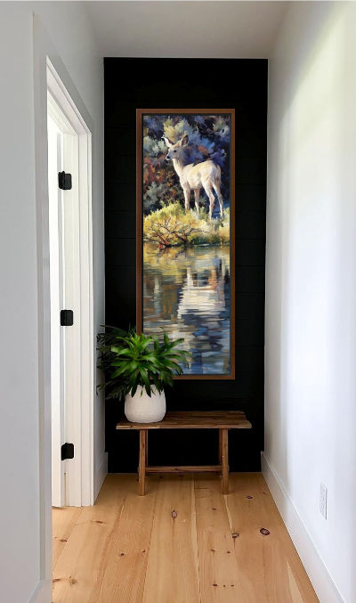 Thumbnail: The same image hanging on a dark wall in a narrow hallway with a door and plant-filled vase on a bench below.