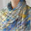 Thumbnail: Cashmere scarf with soft mosaic-inspired pattern in blue, yellow, and gray tones, gracefully draped around the neck.