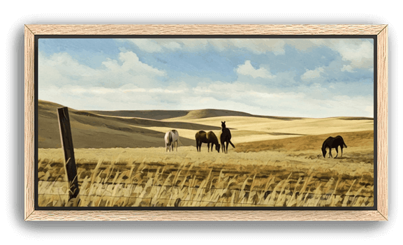 A group of horses graze on a golden hillside beneath a wide blue sky, the scene calm and sunlit, set in an oak frame