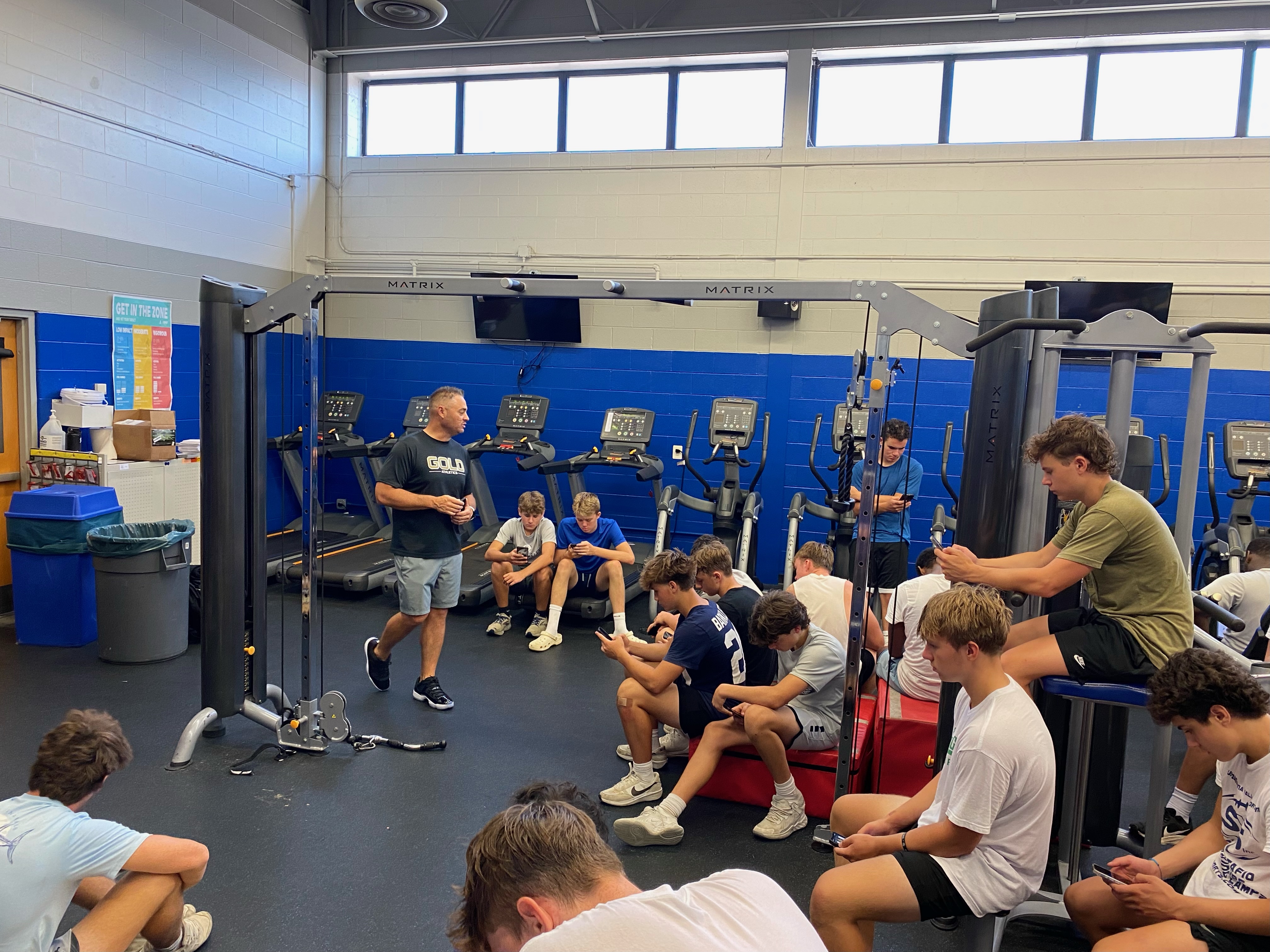 Group of High School Student Athletes listening to a speaker in a gym talking about fundraising with Gold Athletics