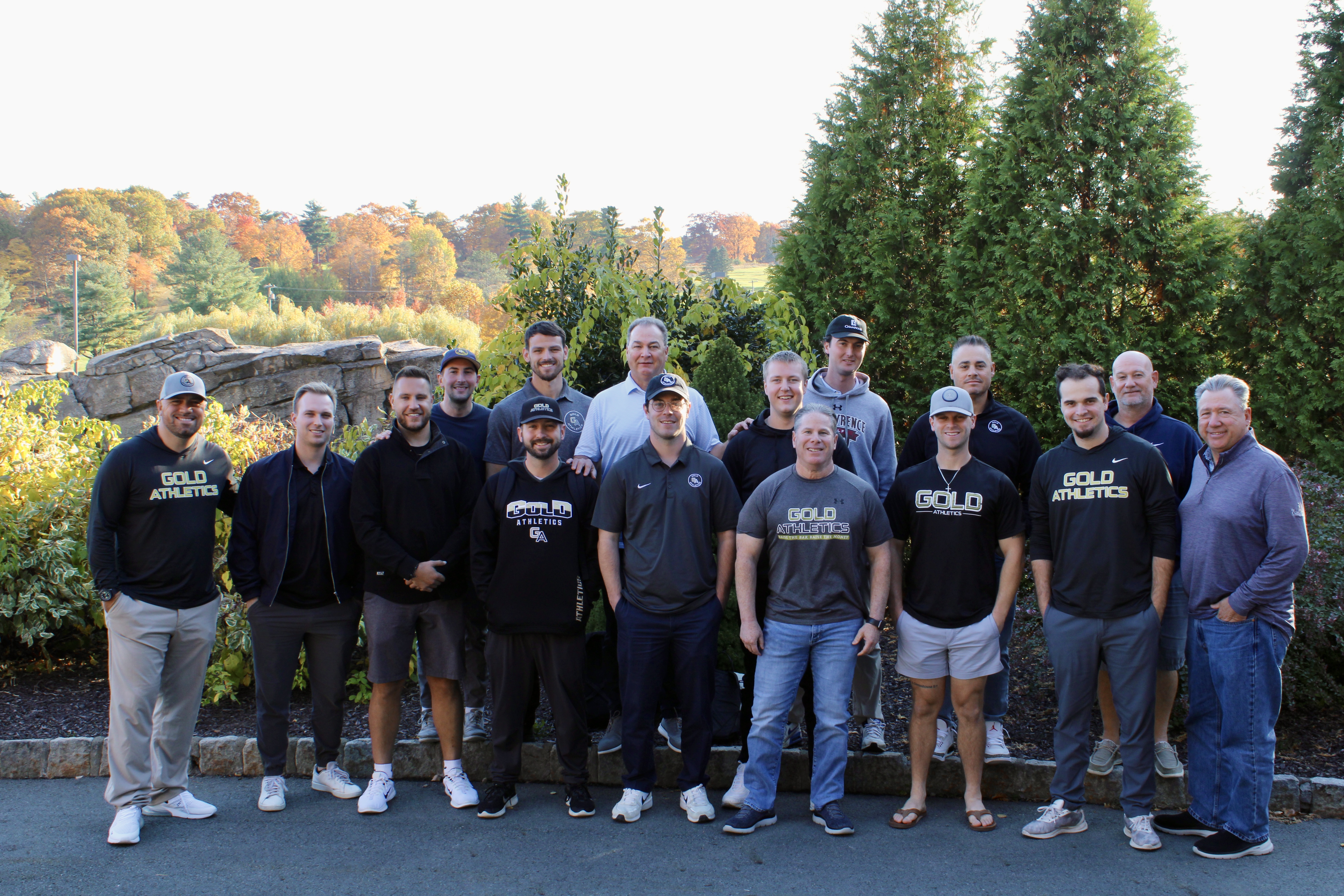 A group of 16 men stands outdoors, many wearing 