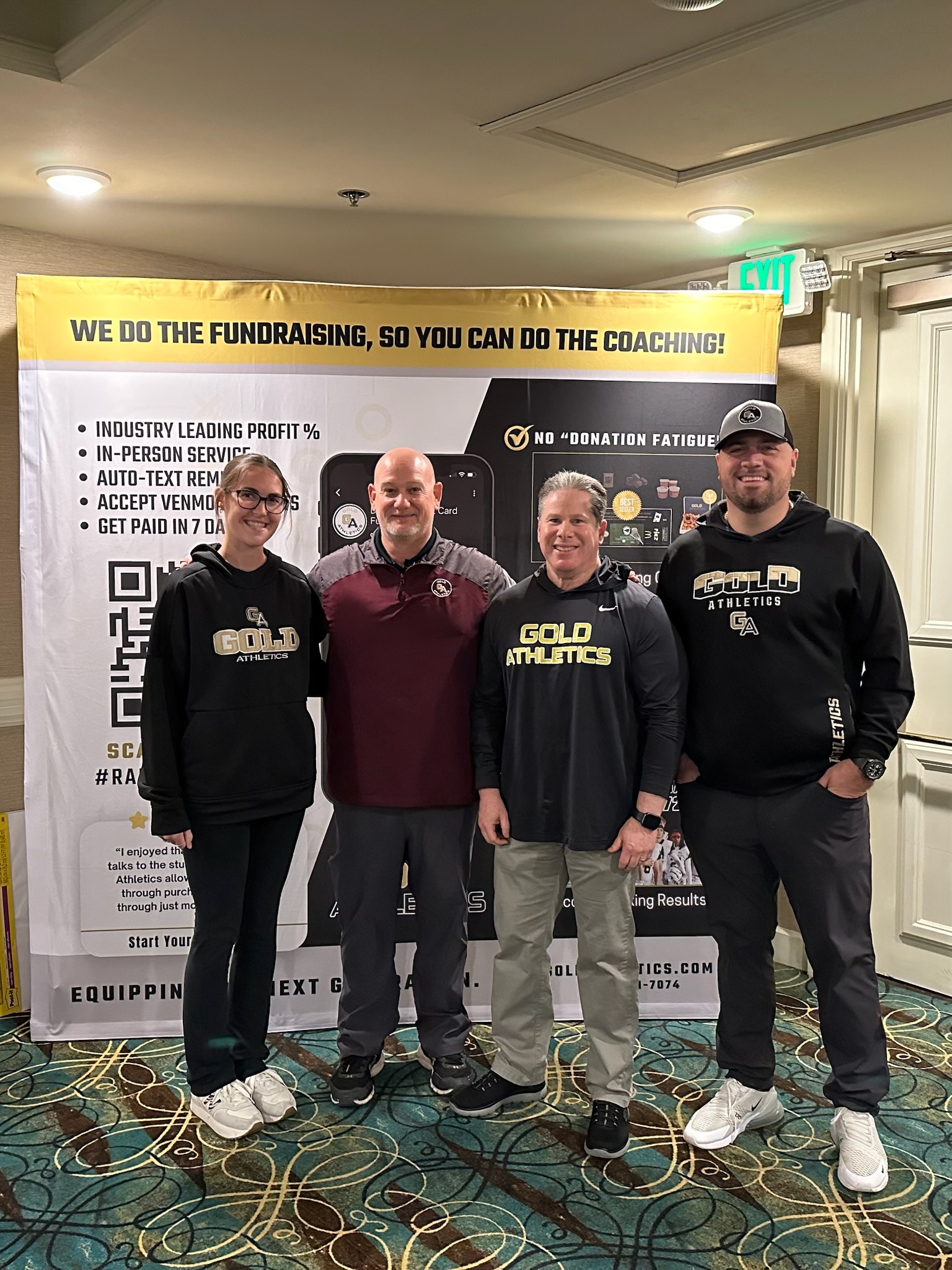 Four people smiling in front of a yellow and black